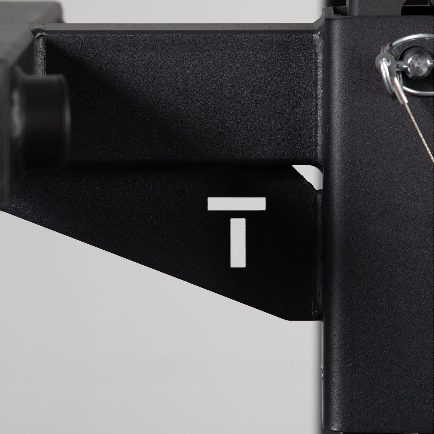 Close-up of a black metal bracket from Titan Fitness X-3 Series Y-Dip Attachment station with a white letter 't' marking, partially obscured, with a visible bolt and shadow detailing. - view 7