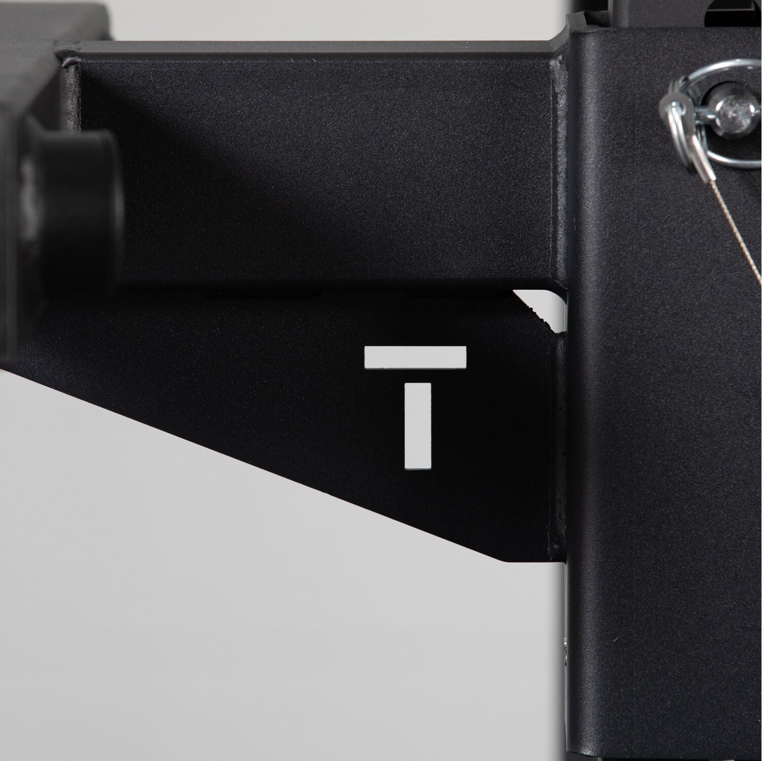 Close-up of a black metal bracket from Titan Fitness X-3 Series Y-Dip Attachment station with a white letter 't' marking, partially obscured, with a visible bolt and shadow detailing.